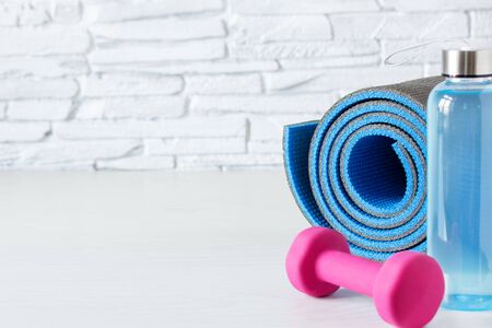 Pink dumbbells, bottle of isotonic drink and fitness mat on white wooden table. Healthy lifestyle concept. Sports.の写真素材