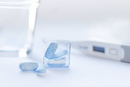 Blue pills on white background with thermometer. Pharmacy concept. Traditional medicine treatment.の写真素材