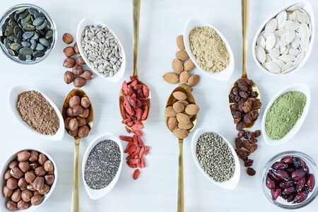 Golden spoons and white bowls with various superfoods on white wooden background top view. Healthy eating concept.の写真素材