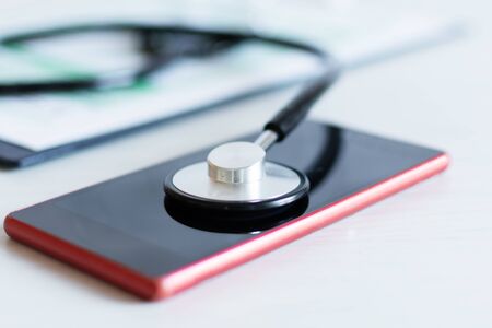 Stethoscope on red smartphone on a grey background. Calling for doctor appointment concept or phone repair service concept.の写真素材