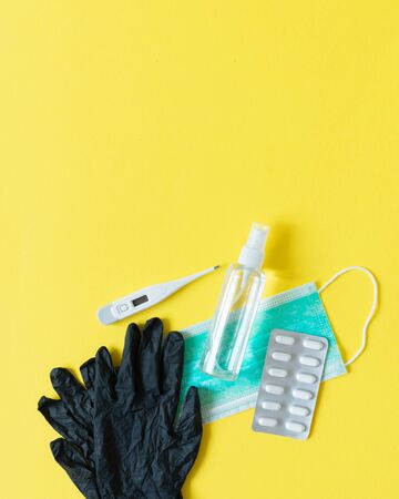 Surgical mask, thermometer, antiseptic and surgical gloves as the virus protection top view on yellow background. Virus illness concept. Cold and flu cure.の写真素材