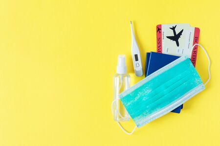 Virus and travel concept. Passport and boarding pass with surgical mask, alcohol sanitizer gel and thermometer on yellow background top view. Protection accessories from virus during traveling.の写真素材