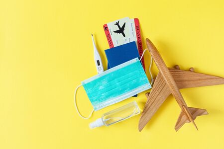 Virus and travel concept. Passport and boarding pass with surgical mask, alcohol sanitizer gel and thermometer on yellow background top view. Protection accessories from virus during traveling.の写真素材