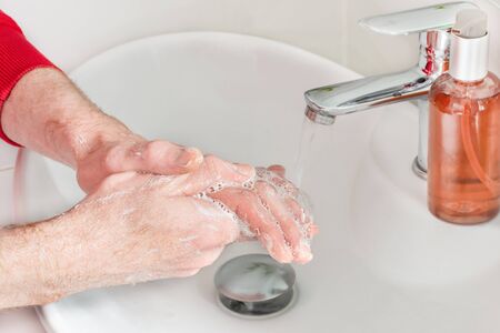 Man washing hands with soap in modern bathroom sinkwith chrome faucet. Flu virus prevention by...