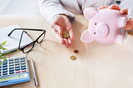 Women counting coins on calculator taking from the piggy bank. Use last savings, unemployment and bankruptcy concept. Crisis and dismissal.の写真素材