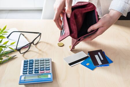 Woman hands with empty wallet, a few coins and credit cards on the table with calculator....