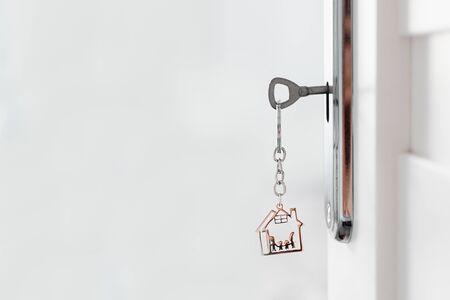 Opened door with key and metal keychain in a house shape. Door to a new house. Real eastate market. Family concept.
