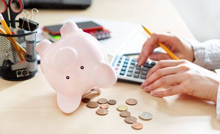 Women counting coins on calculator taking from the piggy bank. Use last savings, unemployment and bankruptcy concept. Crisis and dismissal.の写真素材