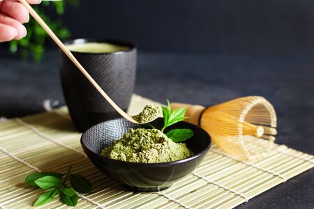 Organic green matcha tea and tea accessories on japanese mat on black background. Japanese tea ceremony concept. Chashaku spoon and chasen bamboo whisk for brewing matcha tea.の写真素材