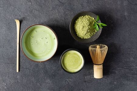 Organic green matcha tea. Matcha powder and matcha tea in a bowl. Chashaku spoon and chasen bamboo whisk for brewing matcha tea top view on black background.の写真素材