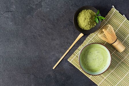 Green matcha tea drink and tea accessories on black background top view. Japanese tea ceremony concept. Chashaku spoon and chasen bamboo whisk for brewing matcha tea.の写真素材