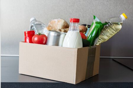 Various food, bottle of oil, milk and water, fresh vegetables in a cardboard box. Food donations or...