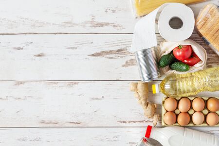 Various food products such as pasta, eggs, canned food, bottle of milk and oil top view on wooden background. Food donation, safe delivery service concept. Grocery shopping.の写真素材
