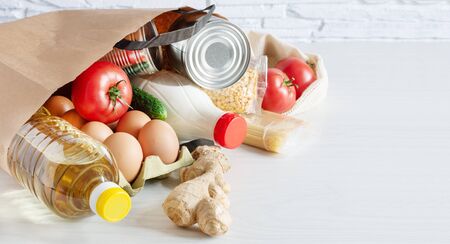 Paper shopping bag with various food. Food donation, safe delivery service concept. Pasta, eggs, canned food, bottle of oil and milk in a grocery shopping bag.の写真素材