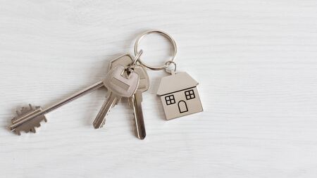 Key and keychain in a house shape on wooden background top view. Real estate concept. Copy space.の写真素材