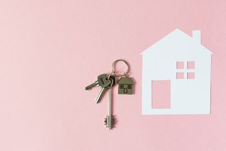 Key and keychain in a house shape and paper model of house on pink background top view. Real estate concept. Copy space.の写真素材