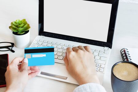 Woman hands holding a credit card and using computer for online shopping entering secure code on keyboard. Blank laptop screen, template for design.の写真素材