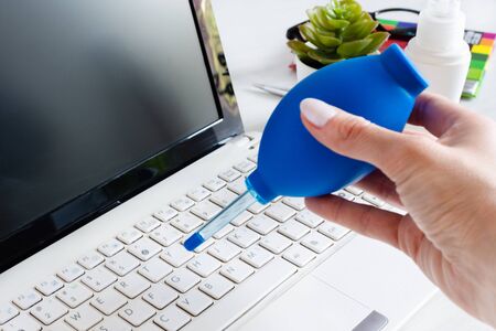 Woman hand sweeping dust from laptop keyboard using air bulb. Computer cleaning with dust blower.の写真素材