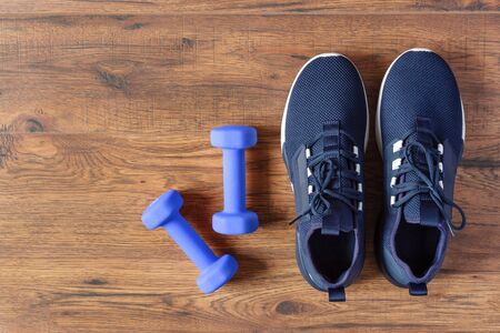 Sport shoes and dumbbells on wooden background top view. Fitness training concept. Copy space.の写真素材