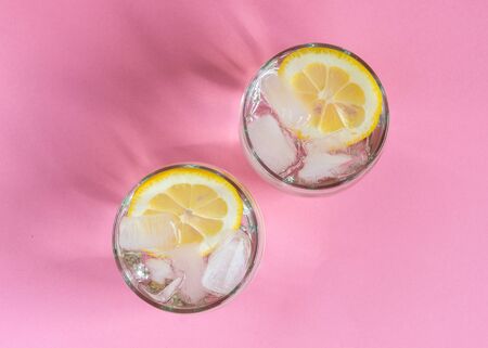 Two glasses of fresh cold water with lemon slices and ice on pastel color background. Healthy lifestyle. Refreshment beverage.の写真素材
