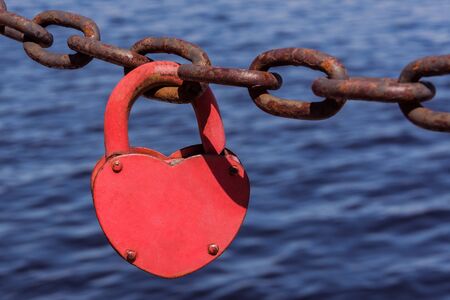 Love heart padlock on the rusty chain on the blue sea water background. Strong love concept.の写真素材