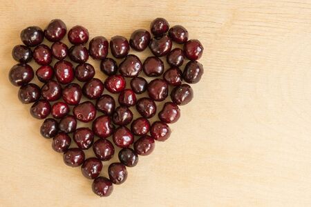 Cherry heart shape on wooden background. Sweet love concept. Copy space.の写真素材