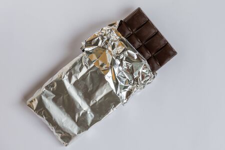 Dark chocolate bar in a foil on white background. Chocolate temptation.の写真素材