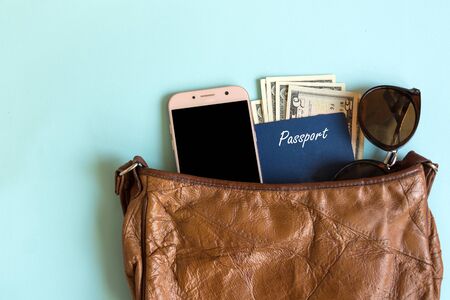 Vintage woman bag with contents for travelling. Passport, smartphone and sunglasses inside the woman...