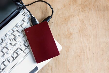 Modern storage, external hard drive and laptop keyboard on wooden table background. Device for many...