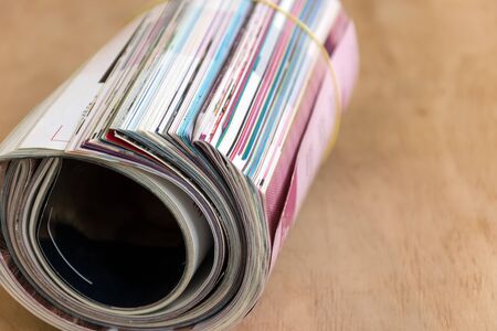 Roll of glossy colorful magazines on wooden background. Mass media. Copy space.