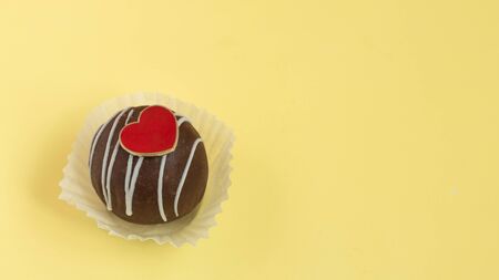 Chocolate muffin with heart candy top view. Sweet cake on pastel yellow background. Copy space.