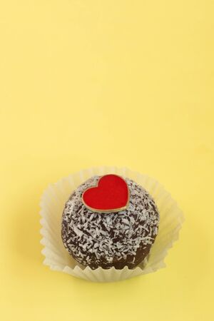 Chocolate muffin with heart candy top view. Sweet cake on pastel yellow background. Copy space.の写真素材