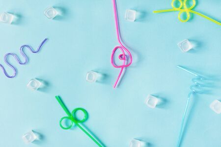 Creative summer background composition with colorful cocktail straws and ice cubes top view on light...