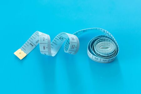 Roled blue measuring tape on blue background. Measuring tape of the tailor. Copy space.