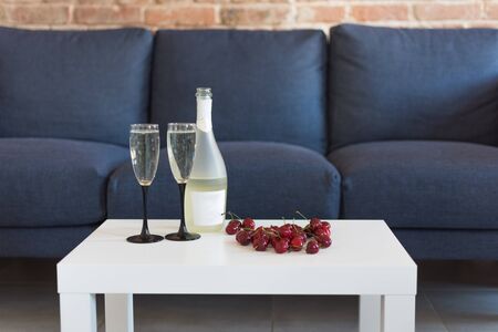 Romantic composition with champagne and cherry. Romantic holiday dinner, a bottle with champagne and two glasses in modern home interior.の写真素材