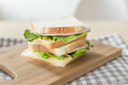 Sandwich with cheese and ham on cutting board on the table in the bright kitchen. Lunch. Sandwich with lettuce. Healthy eating concept.の写真素材