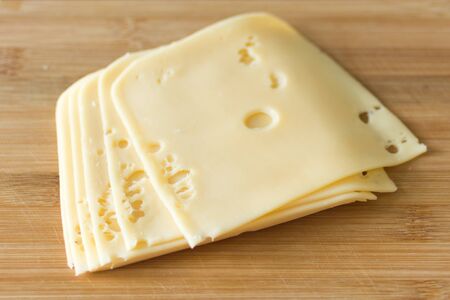 Slices of cheese on wooden background. Holland cheese with holes.