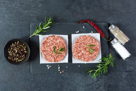 Raw burger cutlets made from minced fresh meet with rosematy and chili on a slate board top view. Ingredients for making burgers.の写真素材