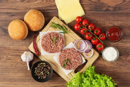 Fresh raw ingredients for homemade burger on wooden background top view. Unhealthy eating, fast food dinner.の写真素材