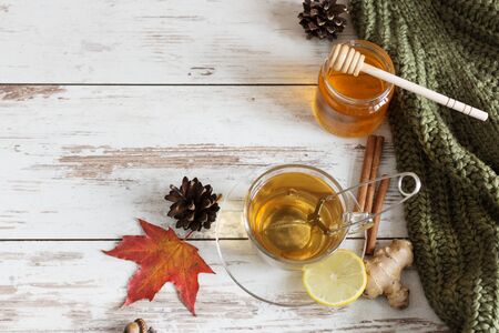 A cup of hot autumn tea with ginger, lemon and cinnamon on wooden background with autumn leaves decoration.の写真素材