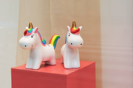 Ceramic souvenir unicorn toy money box with colorful rainbow on pink table.の写真素材