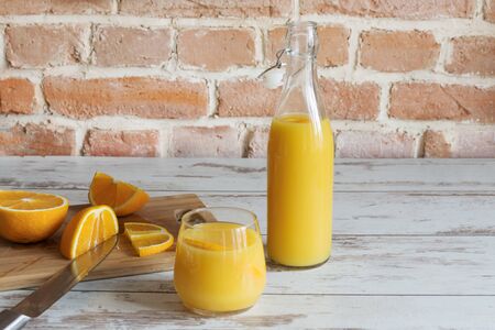 Freshly squeezed orange juice standing on wooden table on brick wall background with fresh oranges.