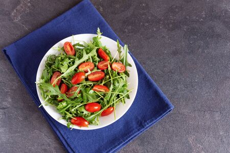 Salad with fresh green arugula and tomato cherry in a white ceramic bowl. Arugula is rich in vitamins and trace elements.の写真素材