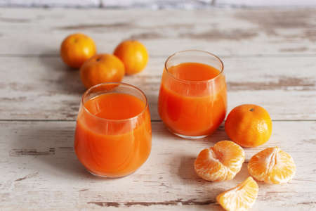 Glass of fresh tangerine juice with ripe tangerines on wooden table background. Healthy vitamins beverage.の写真素材