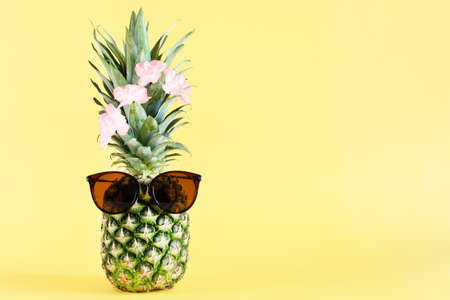 Funny pineapple with sunglasses on yellow pastel background. Summer background. Copy space.