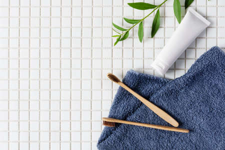 Bamboo toothbrush, toothpaste and towel on white mosaic background top view. Dental hygiene concept....