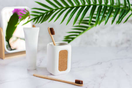 Bamboo toothbrushes in a cup, toothpaste and mirror on white marble table in a bathroom. Sustainable lifestyle, dental hygiene concept.の写真素材
