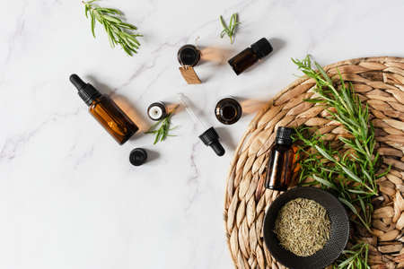 Bottles of rosemary essential oil and fresh rosemary branch on white marble background top view.の写真素材