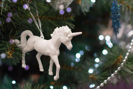 White shiny toy unicorn on Christmas tree. Christmas tree with decoration and bright bokeh. Greeting Christmas card.の写真素材