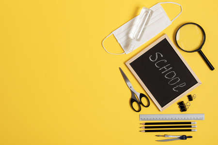 Blackboard with school and office supplies on yellow background top view during coronavirus time. Back to school concept. Copy space.の写真素材